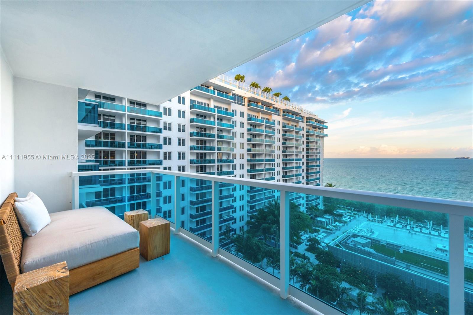 A balcony features a daybed, wooden side tables, and a view of the ocean — 102 24th St # 1144, Miami Beach FL 33139, MIAMI BEACH, FL