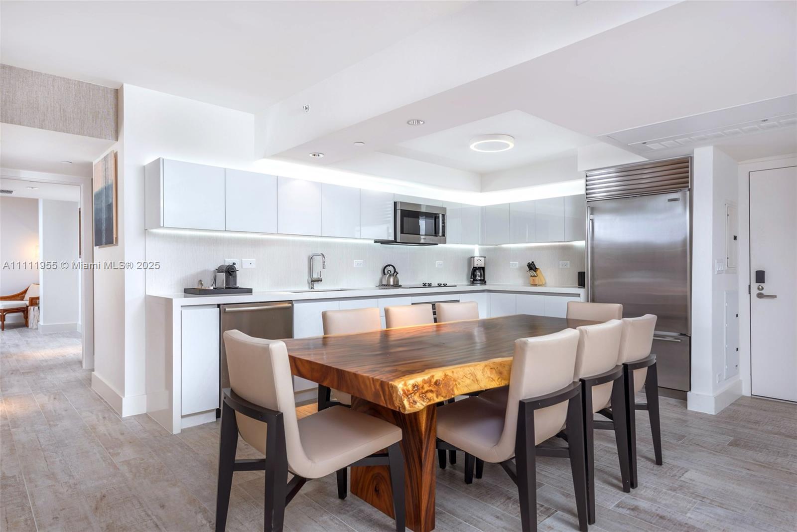 A modern kitchen features white cabinetry, stainless steel appliances, and a live-edge wood dining table — 102 24th St # 1144, Miami Beach FL 33139, MIAMI BEACH, FL