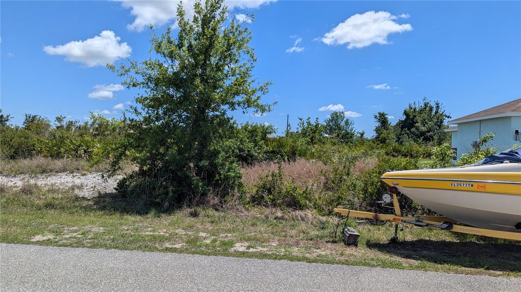 A vacant lot with a large tree and brush sits next to a parked boat — 13485 ABUTILON LANE, PORT CHARLOTTE, FL