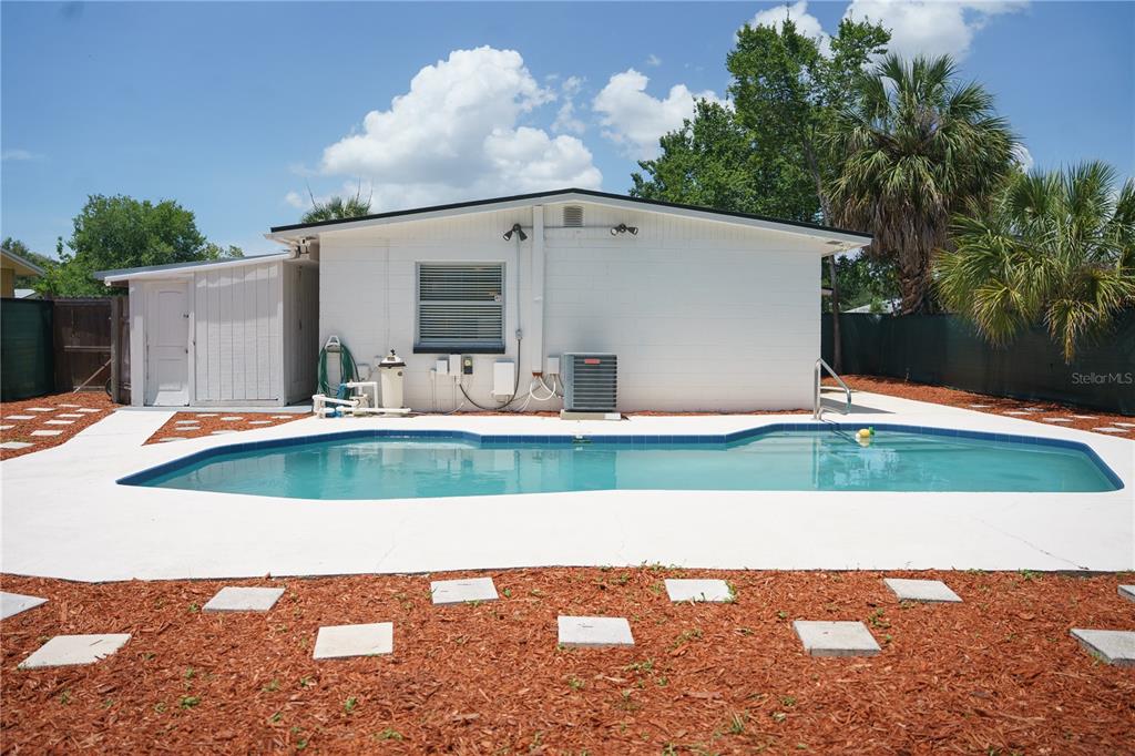 A backyard features a swimming pool, a white house exterior, and a mulched area with pavers — 6552 S WEST SHORE CIRCLE, TAMPA, FL