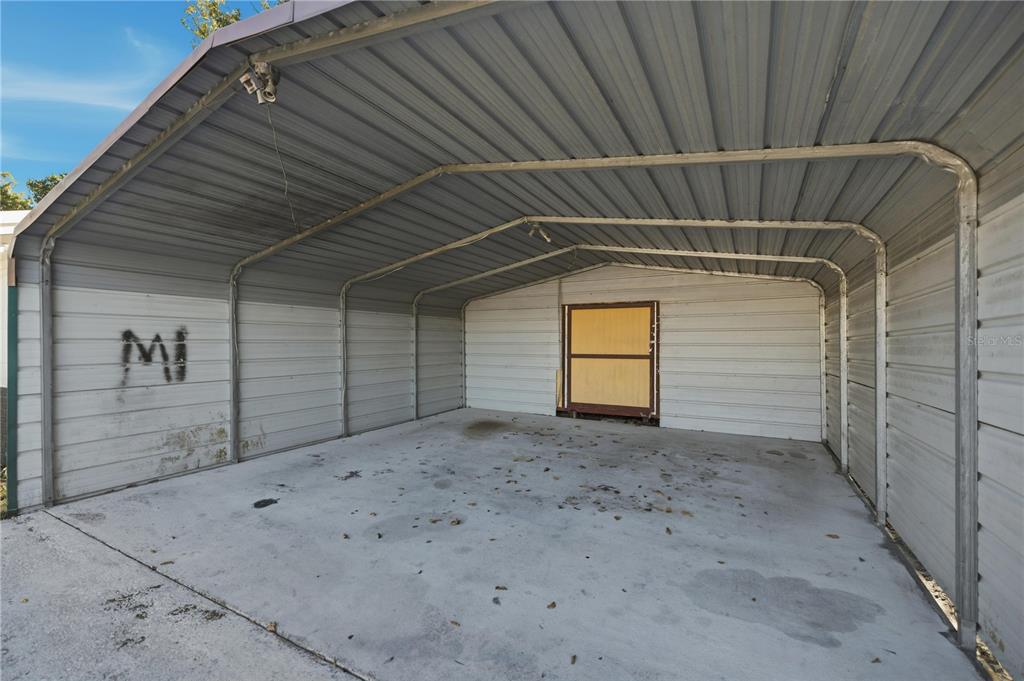 An open-sided metal carport with a concrete floor and a small yellow door at back — 1915 BRONSON STREET, PALATKA, FL