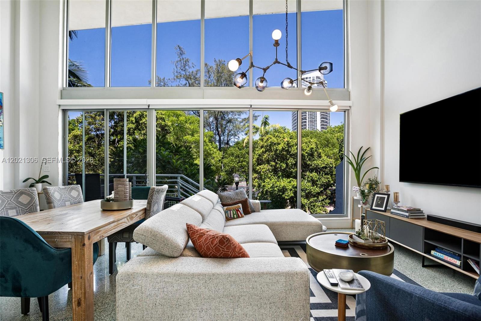 A modern living and dining area features floor-to-ceiling windows, a sectional sofa, and chandelier — 245 Michigan Ave # 5, Miami Beach FL 33139, MIAMI BEACH, FL
