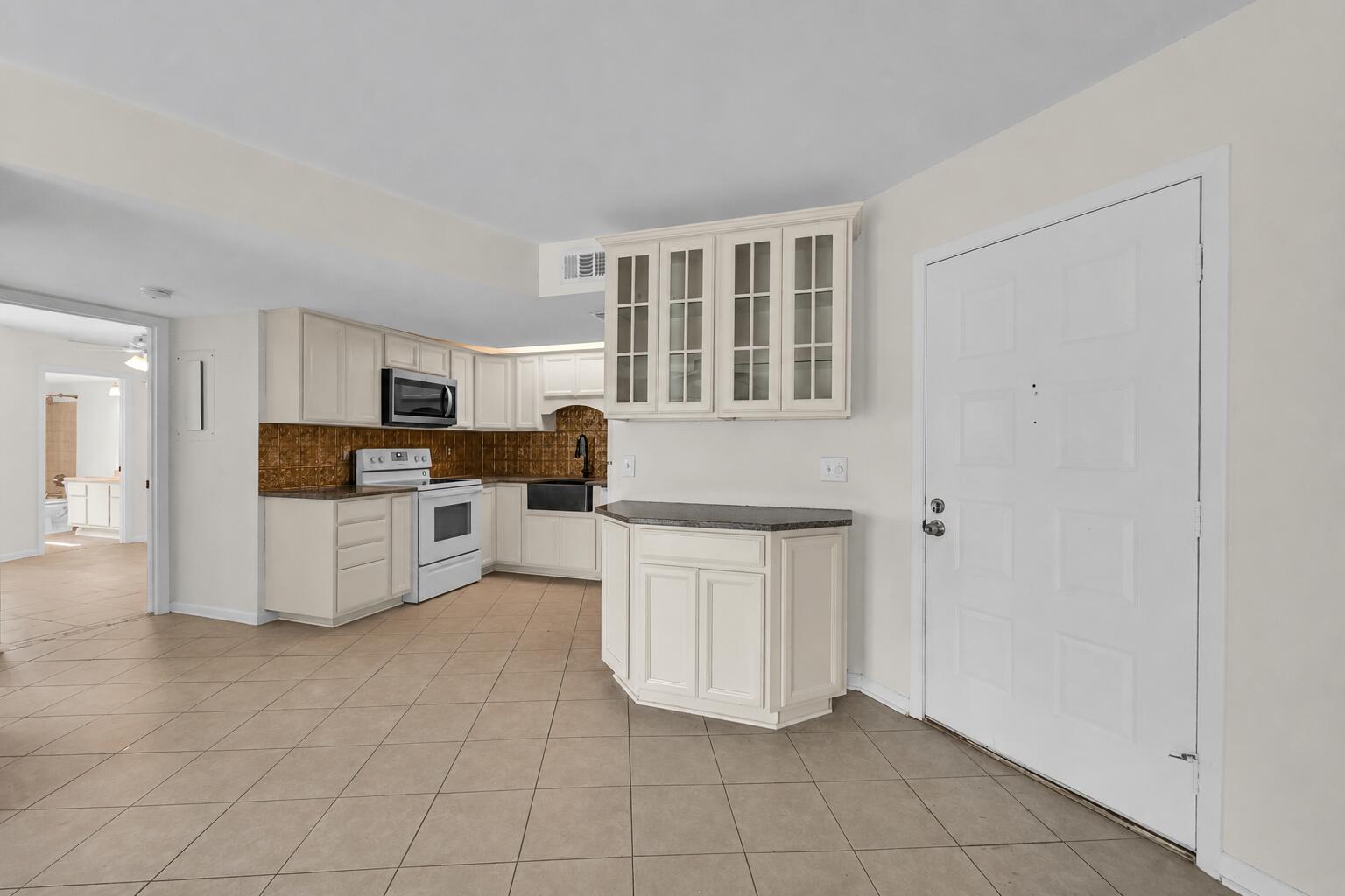 A kitchen with white cabinets, dark countertops, a tiled backsplash, and light-colored floor tiles — 2013 NE Collins Circle # 50, Jensen Beach FL 34957, JENSEN BEACH, FL