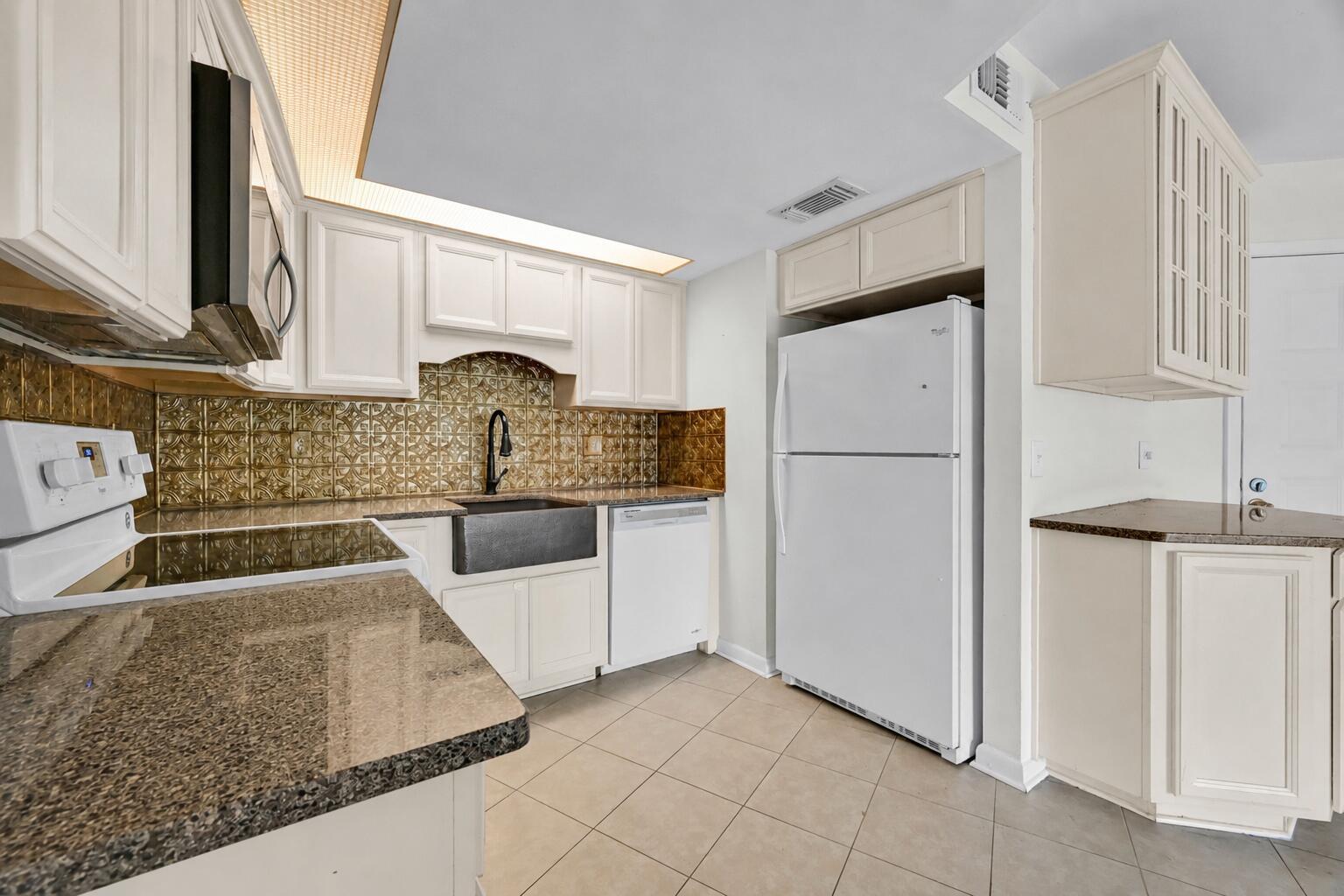 A kitchen features white cabinets, granite countertops, a farmhouse sink, and a metallic backsplash — 2013 NE Collins Circle # 50, Jensen Beach FL 34957, JENSEN BEACH, FL