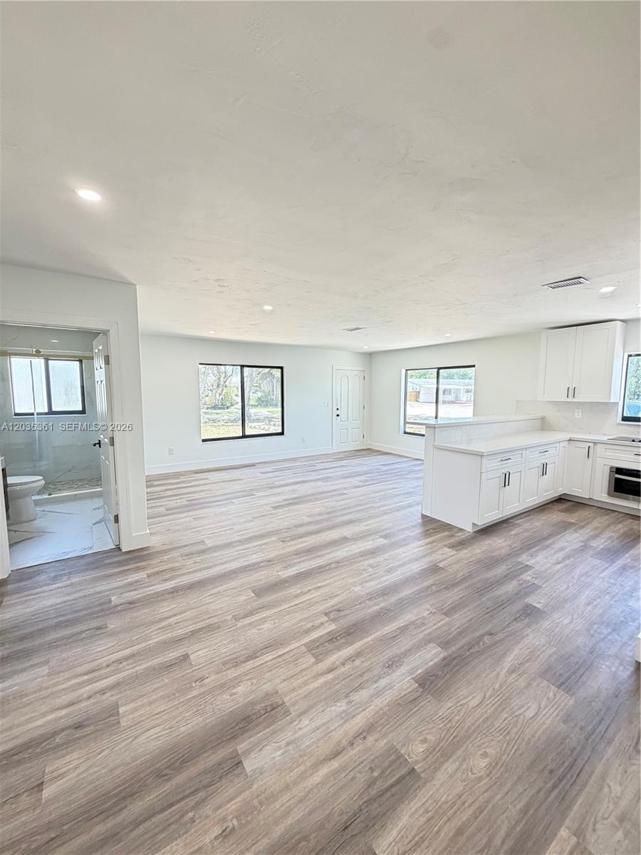 This open-concept living area features light wood-look flooring, white kitchen cabinetry, and a bathroom entrance — 2930 SW 106th Ave, Miami FL 33165, MIAMI, FL