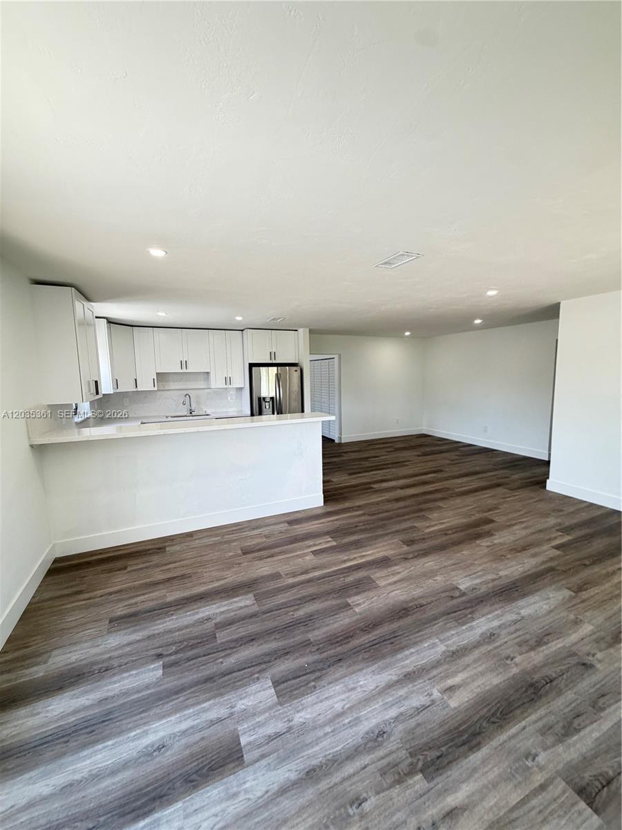 An open-concept kitchen and living area features white cabinets, a breakfast bar, and wood-look flooring — 2930 SW 106th Ave, Miami FL 33165, MIAMI, FL
