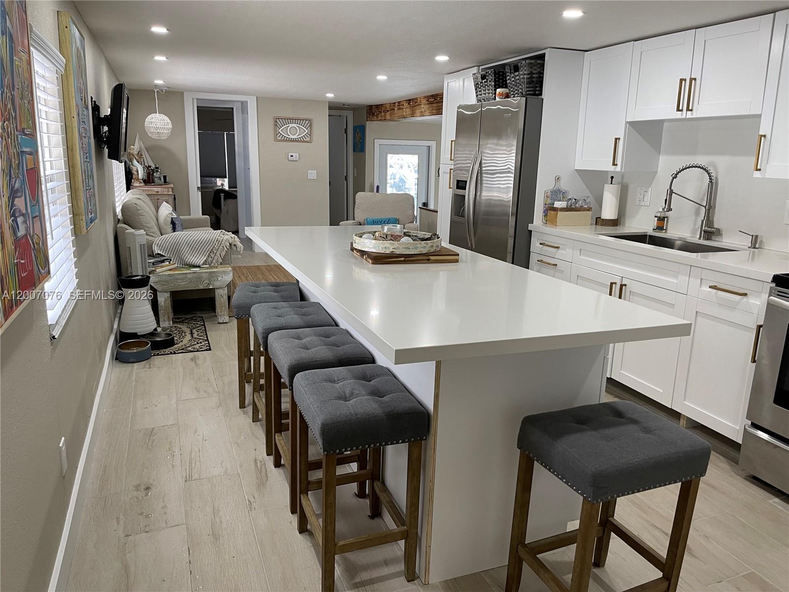 A modern kitchen features a large white island with grey stools and stainless steel appliances — 721 Garden State Ln, Key Largo FL 33037, KEY LARGO, FL