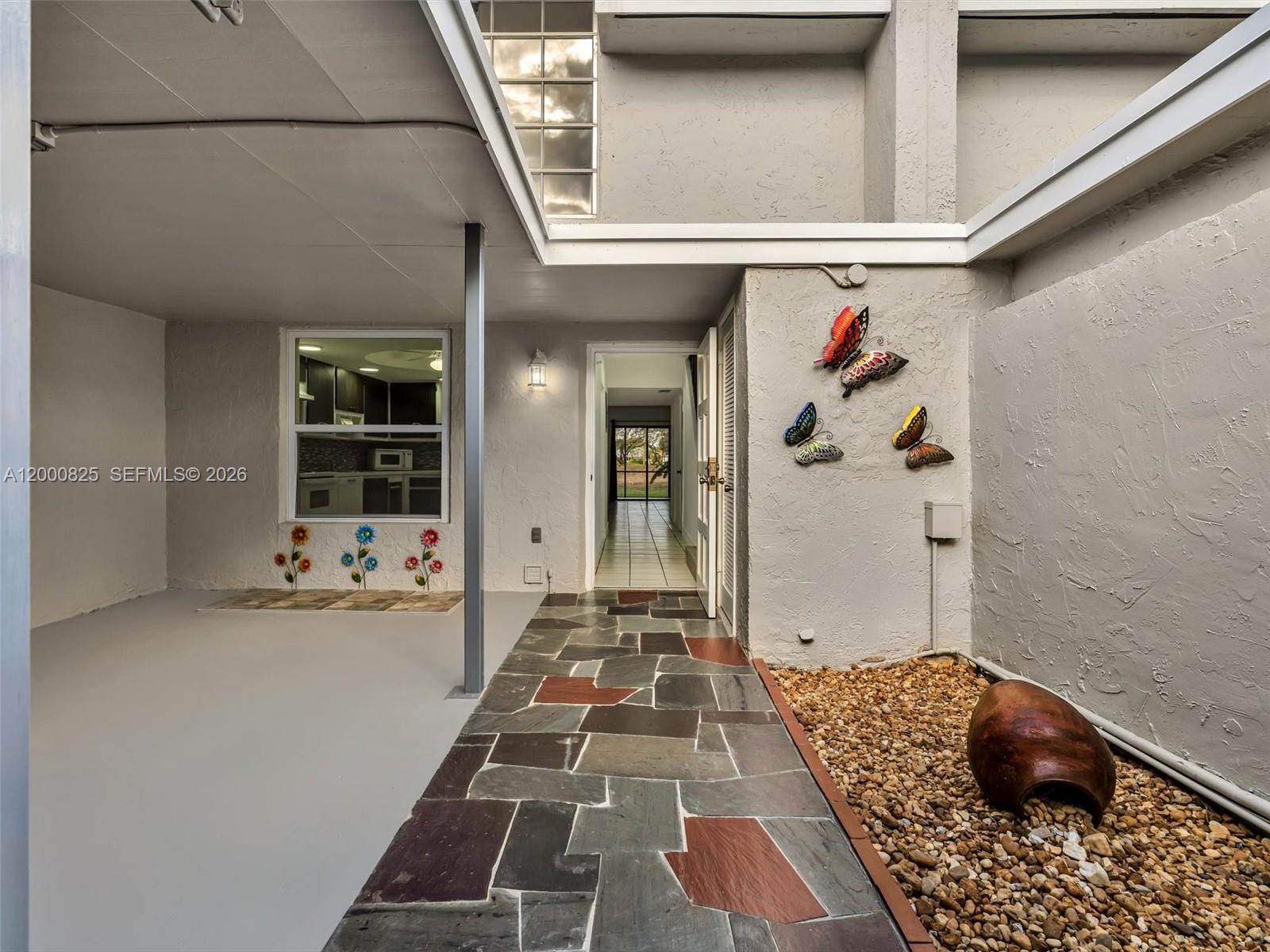 An outdoor entryway features a stone walkway, a gravel garden, and butterfly wall decor — 19174 Bobolink Dr, Hialeah FL 33015, HIALEAH, FL