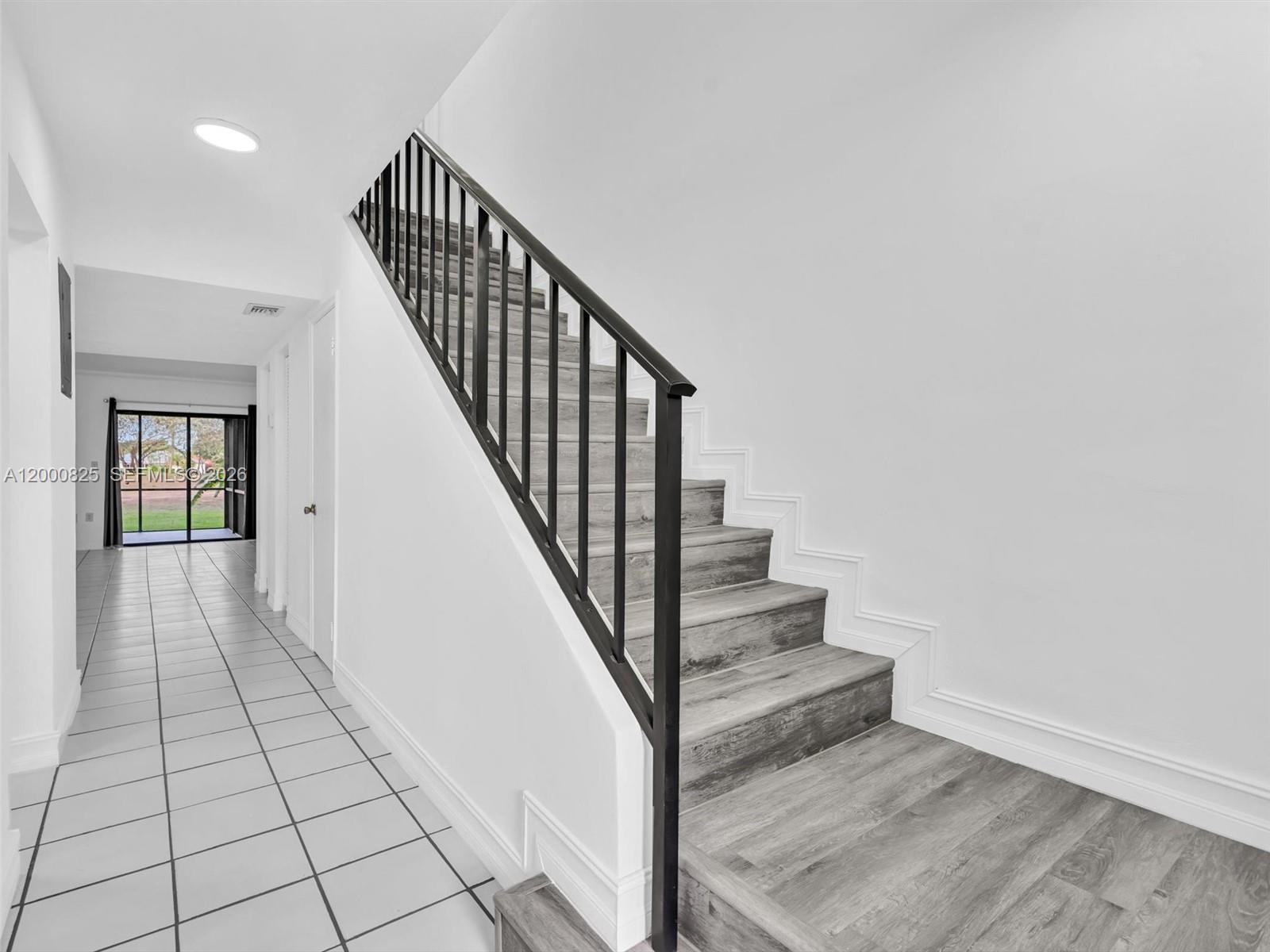 A staircase with wood-look steps and a black metal railing leads to an upper floor — 19174 Bobolink Dr, Hialeah FL 33015, HIALEAH, FL