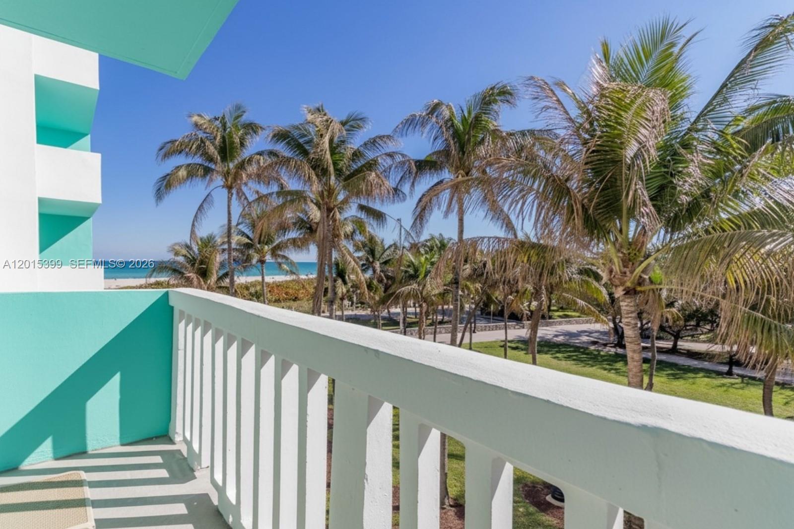 A balcony with a white railing overlooks palm trees, a grassy area, and the ocean — 301 Ocean Dr # 306, Miami Beach FL 33139, MIAMI BEACH, FL