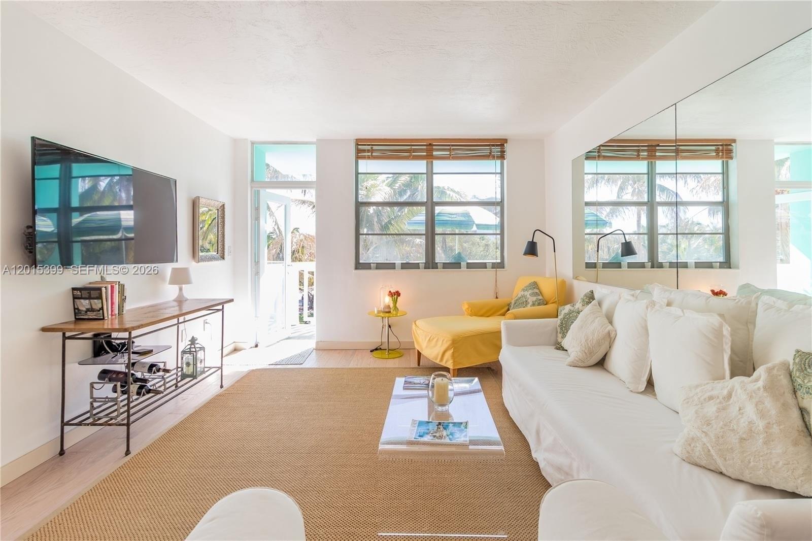 A living room features a white sofa, yellow chaise, television, and a large wall mirror — 301 Ocean Dr # 306, Miami Beach FL 33139, MIAMI BEACH, FL