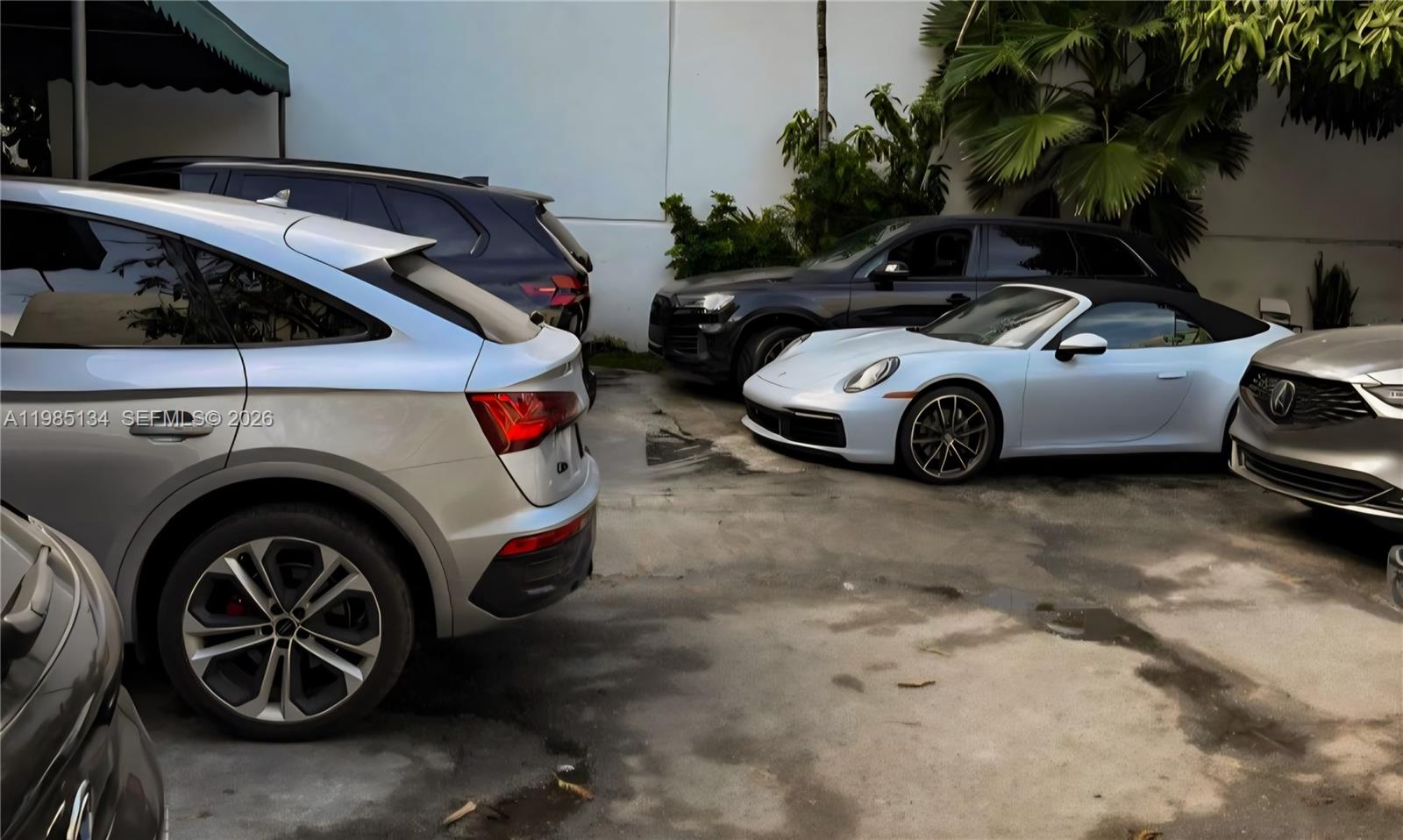 Several luxury vehicles are parked in a paved outdoor lot near a white wall — 0000 Bay Rd, Miami Beach FL 33139, MIAMI BEACH, FL
