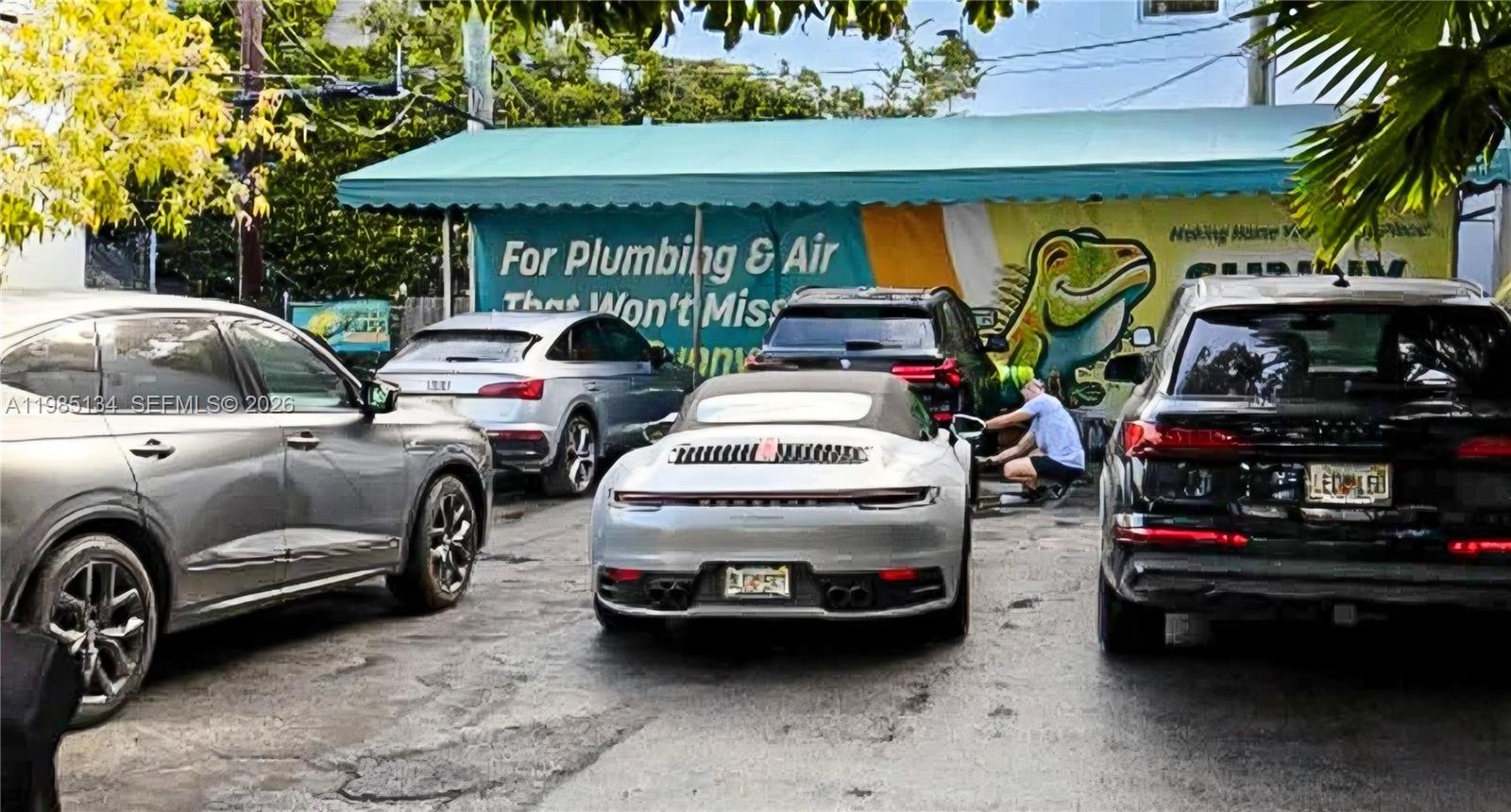 A parking area features several luxury cars parked in front of a building with signage — 0000 Bay Rd, Miami Beach FL 33139, MIAMI BEACH, FL