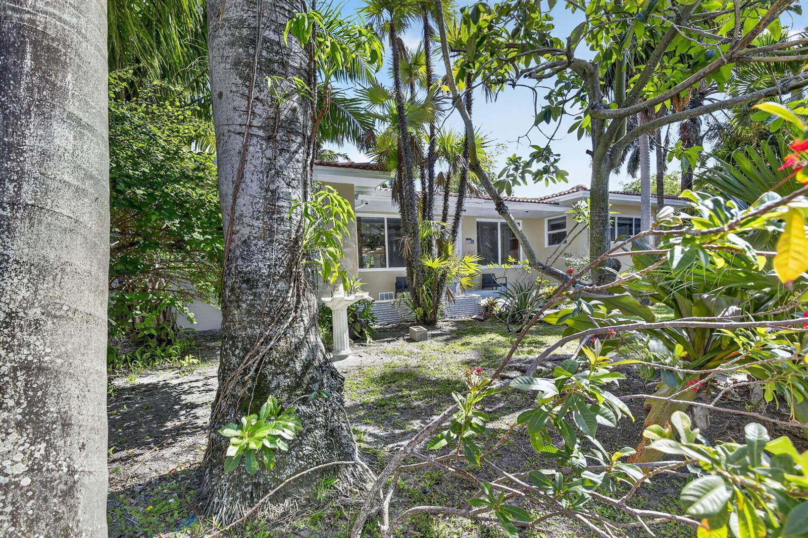 A view of a single-story house exterior from a shaded, tree-filled yard — 742 Hollywood Boulevard, Hollywood FL 33019, HOLLYWOOD, FL