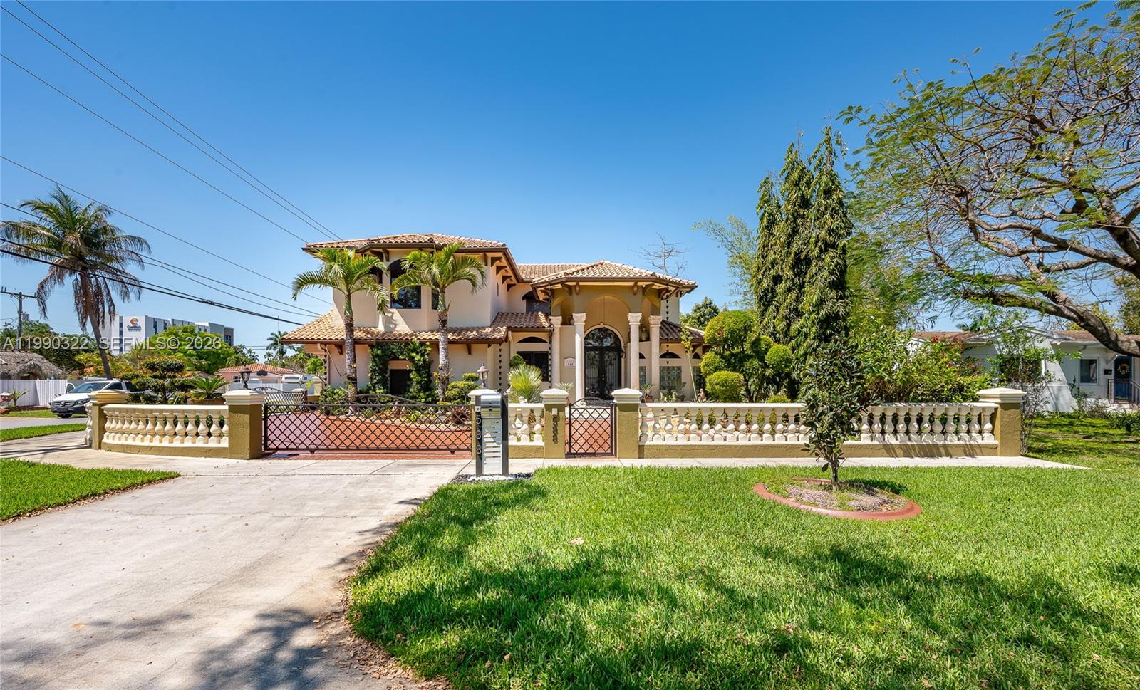A two-story Mediterranean-style house features a gated driveway, a balustrade fence, and palm trees — 588 Miller Dr, Miami Springs FL 33166, MIAMI SPRINGS, FL