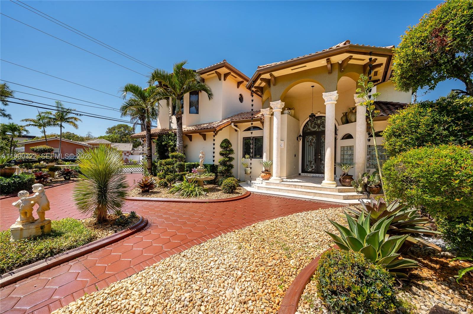 A two-story Mediterranean-style house features a red paved driveway, stone columns, and lush landscaping — 588 Miller Dr, Miami Springs FL 33166, MIAMI SPRINGS, FL