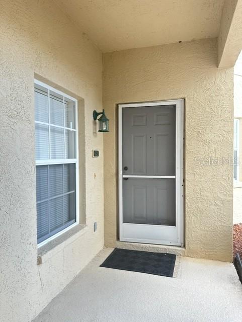 A beige stucco entryway features a window with blinds and a grey storm door — 5800 SABAL TRACE DRIVE UNIT 603, NORTH PORT, FL