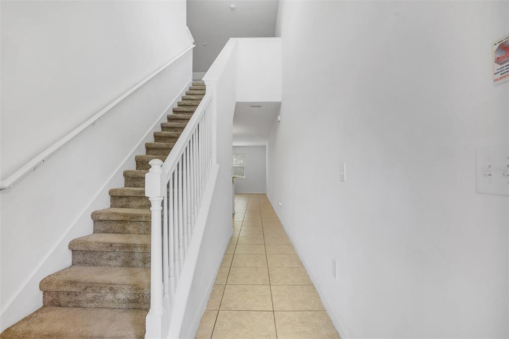 A carpeted staircase with a white railing sits beside a tiled hallway leading to a window — 3610 RODRICK CIRCLE, ORLANDO, FL