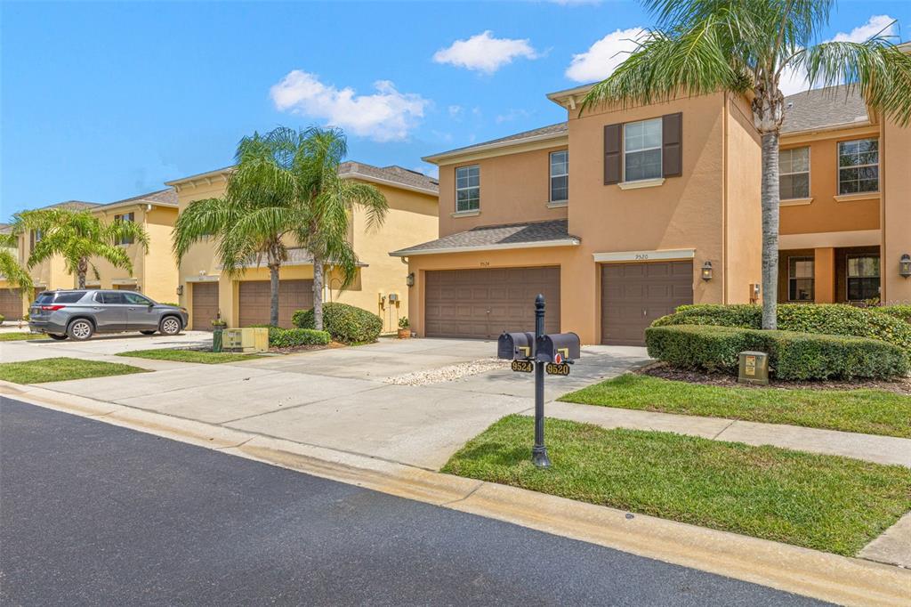 Two-story townhouses with tan stucco exteriors, brown garage doors, and palm trees in the front — 9524 TRUMPET VINE LOOP, NEW PORT RICHEY, FL