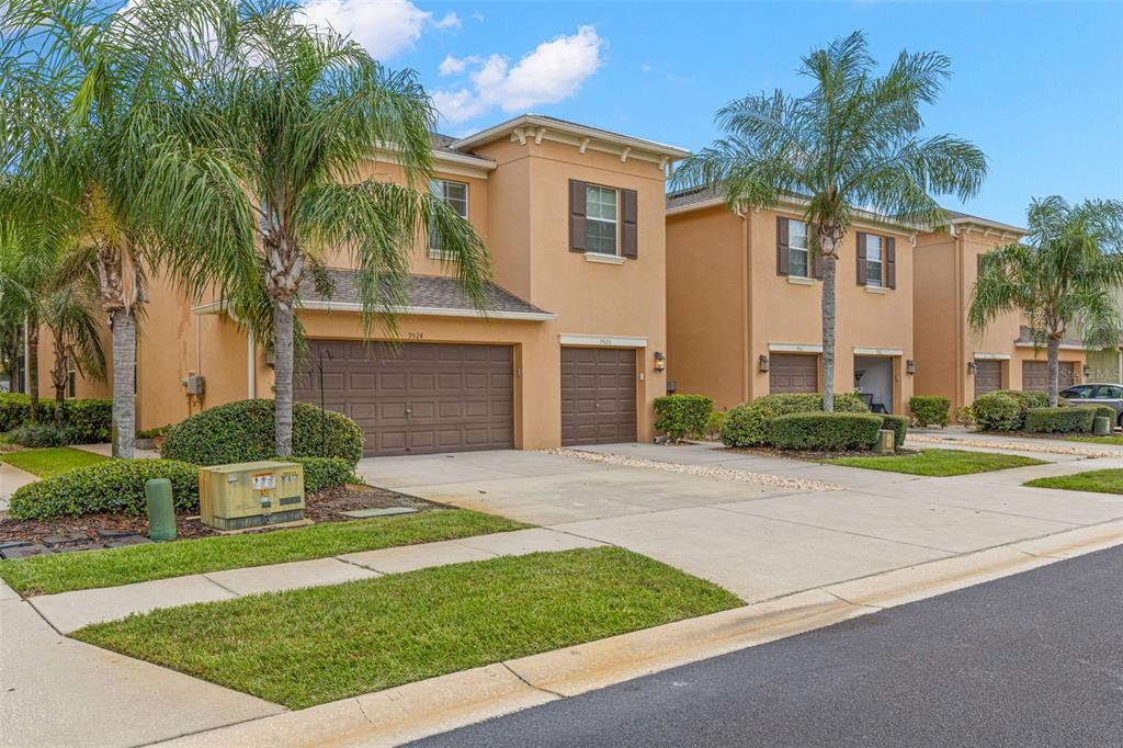 A row of two-story tan stucco townhomes with brown garage doors and palm trees — 9524 TRUMPET VINE LOOP, NEW PORT RICHEY, FL