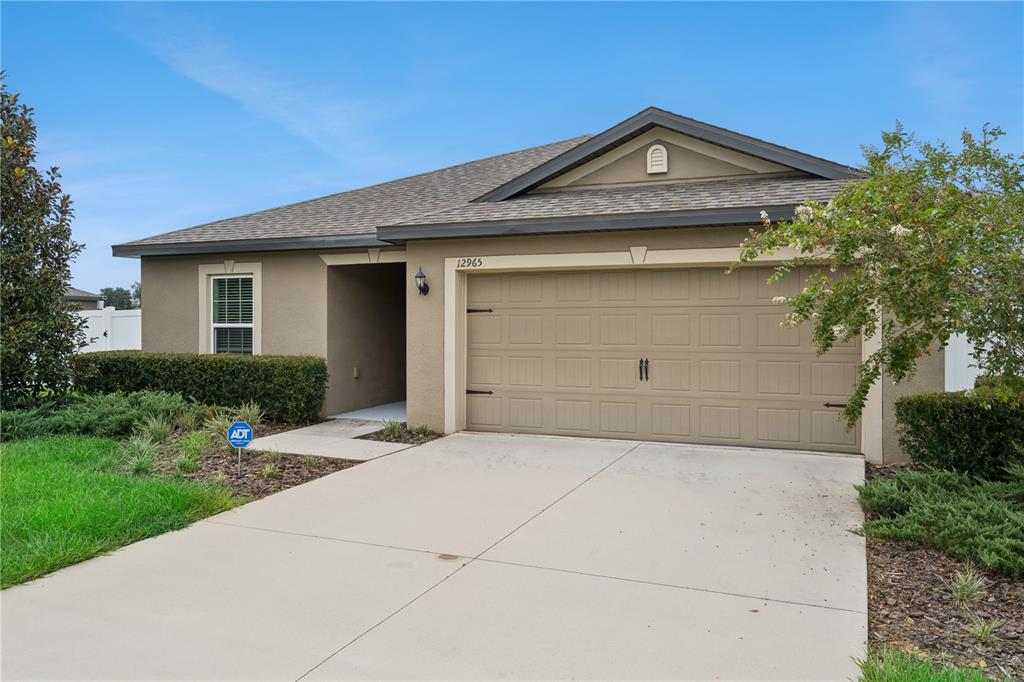 A single-story house with a tan stucco exterior, a two-car garage, and a concrete driveway — 12965 DEL LAGO DRIVE, ASTATULA, FL