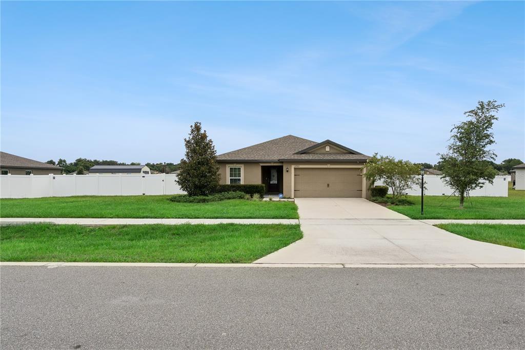 A single-story house with a tan exterior, a two-car garage, and a white privacy fence — 12965 DEL LAGO DRIVE, ASTATULA, FL