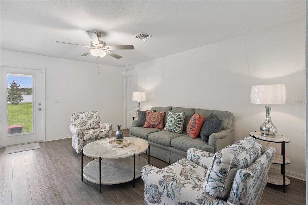A living room features a gray sofa, two patterned armchairs, a coffee table, and wood-look flooring — 12965 DEL LAGO DRIVE, ASTATULA, FL