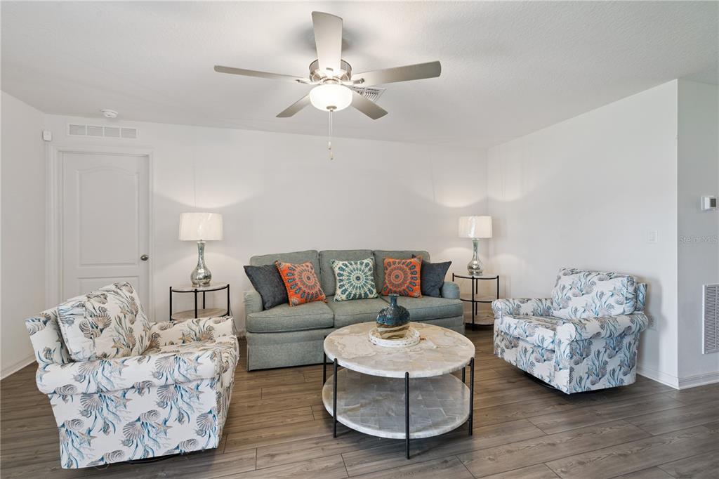 A living room features a sofa, two patterned armchairs, a coffee table, and a ceiling fan — 12965 DEL LAGO DRIVE, ASTATULA, FL