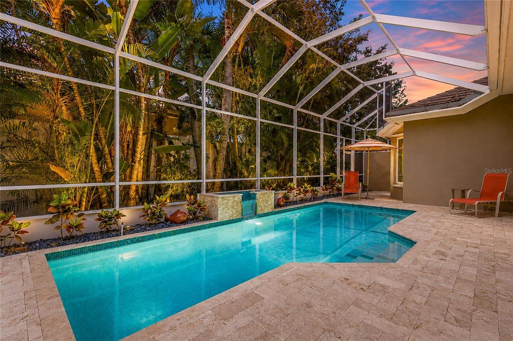 A screened-in swimming pool with a stone water feature and patio furniture at sunset — 8762 52ND AVENUE E, BRADENTON, FL