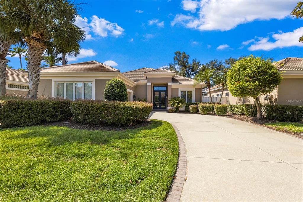 A single-story house with a concrete driveway, manicured hedges, and palm trees under a sky — 8762 52ND AVENUE E, BRADENTON, FL