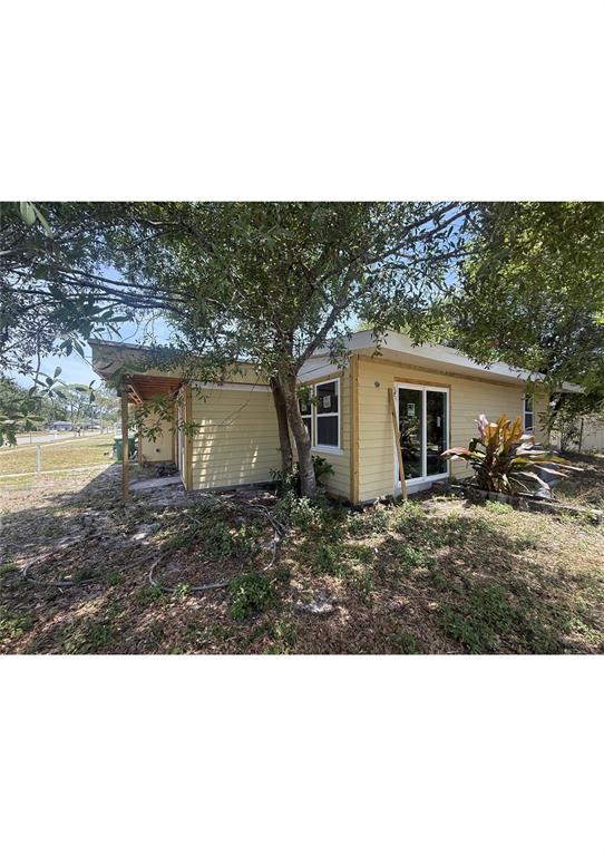A yellow house exterior features a covered porch, sliding glass doors, and a large tree — 4730 W WALLACE AVENUE, TAMPA, FL