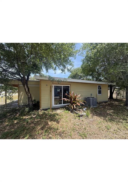 A yellow single-story house exterior features a sliding glass door, an air conditioning unit, and trees — 4730 W WALLACE AVENUE, TAMPA, FL