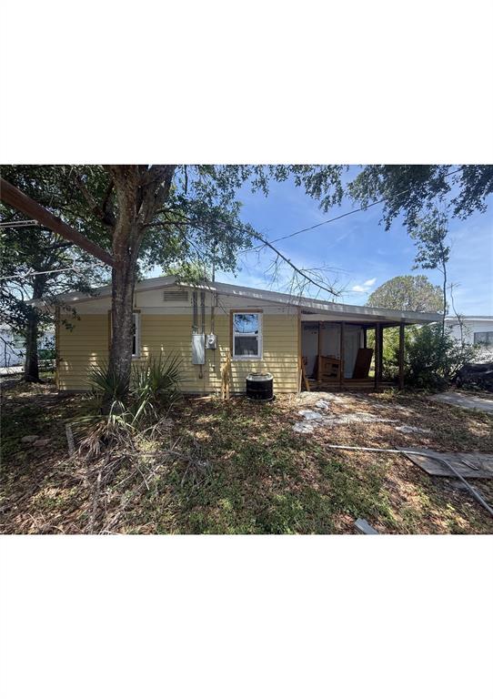 The exterior of a yellow, single-story house features a partially enclosed porch and a tree — 4730 W WALLACE AVENUE, TAMPA, FL