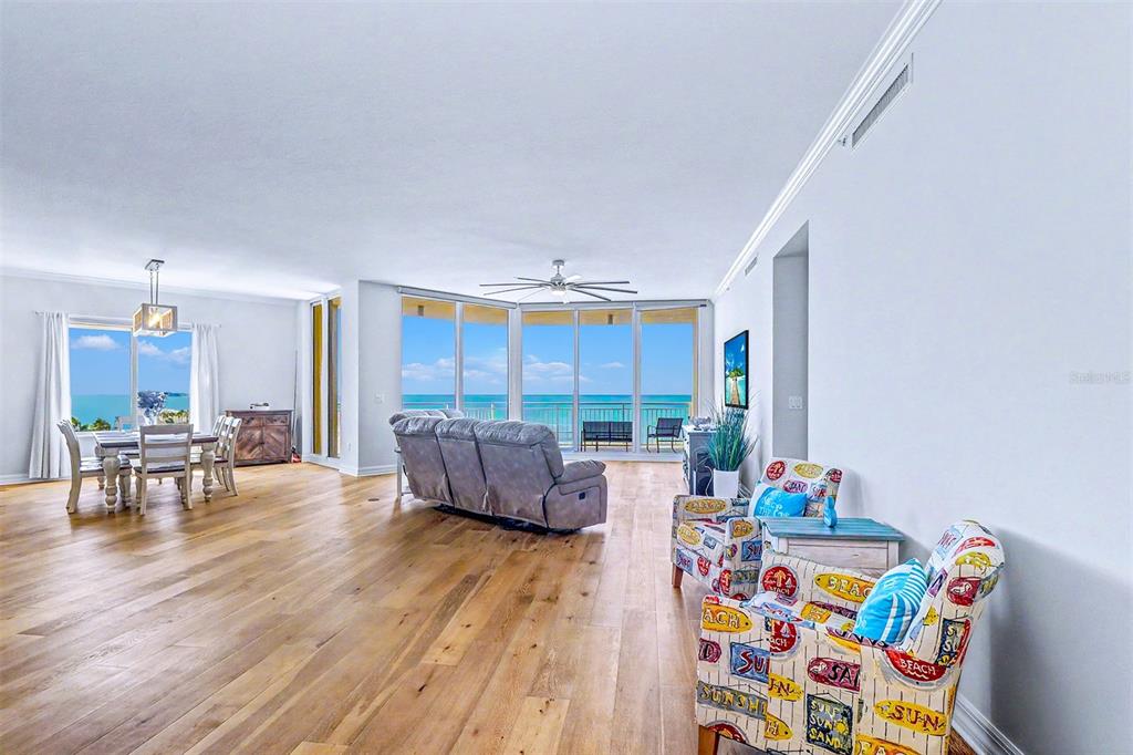 A living and dining area features wood floors, a gray sofa, and floor-to-ceiling ocean views — 15208 GULF BOULEVARD UNIT 601, MADEIRA BEACH, FL