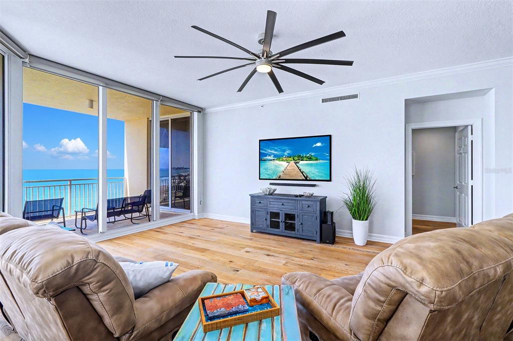 A living room with wood floors, a ceiling fan, a television, and a balcony view — 15208 GULF BOULEVARD UNIT 601, MADEIRA BEACH, FL