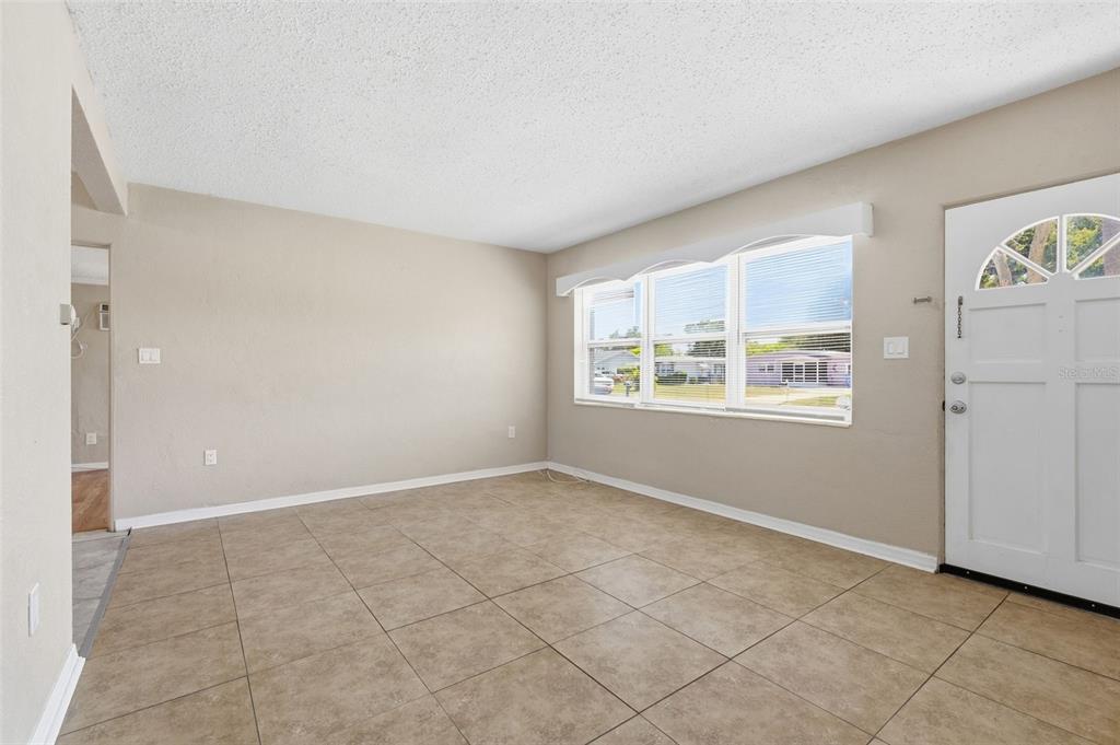 An empty living room features beige walls, large windows, and light-colored tile flooring — 8871 93RD STREET, SEMINOLE, FL
