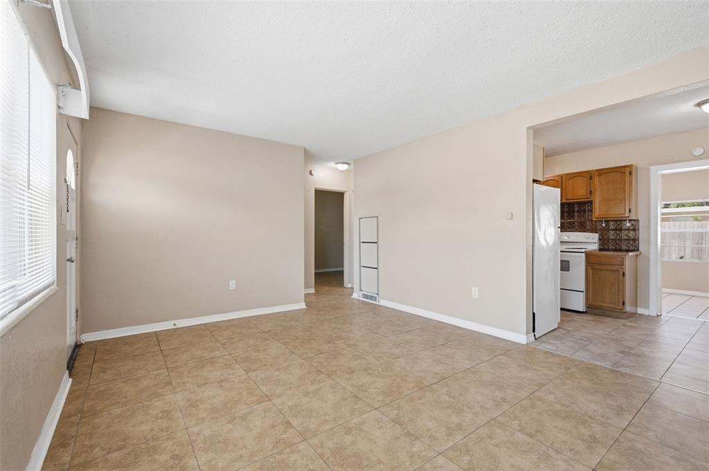 An empty room with tan tile flooring leads to a kitchen with wooden cabinets — 8871 93RD STREET, SEMINOLE, FL