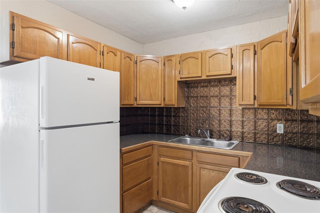 A kitchen features wood cabinets, a white refrigerator, a white stove, and a metallic backsplash — 8871 93RD STREET, SEMINOLE, FL