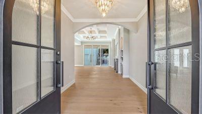 A view through arched double doors into a bright foyer with light wood flooring — 1850 WEBBER STREET, SARASOTA, FL