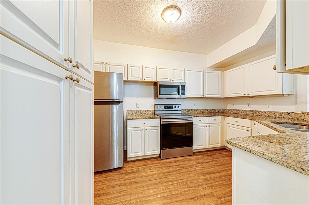 A kitchen features white cabinets, granite countertops, stainless steel appliances, and wood-look flooring — 5500 METROWEST BOULEVARD UNIT 14-203, ORLANDO, FL