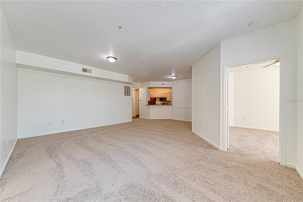 A spacious living room with beige carpet, white walls, and an open kitchen view — 5500 METROWEST BOULEVARD UNIT 14-203, ORLANDO, FL