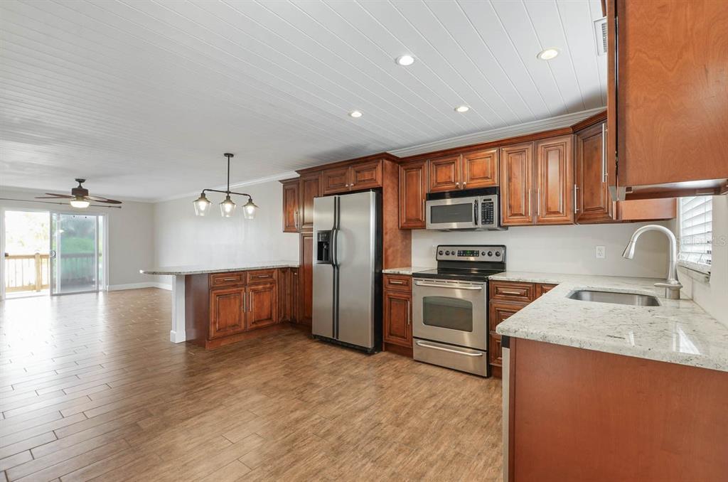 A kitchen with dark wood cabinets, stainless steel appliances, and granite countertops opens to a room — 6506 ABACO DRIVE UNIT 104, APOLLO BEACH, FL