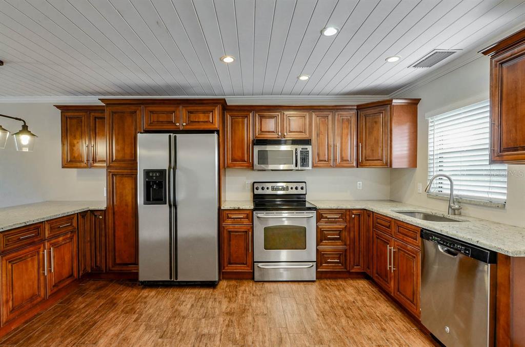 A kitchen with wood cabinets, stainless steel appliances, granite countertops, and a white plank ceiling — 6506 ABACO DRIVE UNIT 104, APOLLO BEACH, FL