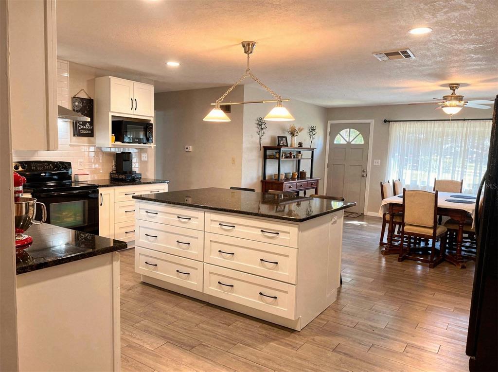 A kitchen with white cabinets, a dark granite island, and wood-look flooring — 2009 NE 51ST PLACE, OCALA, FL