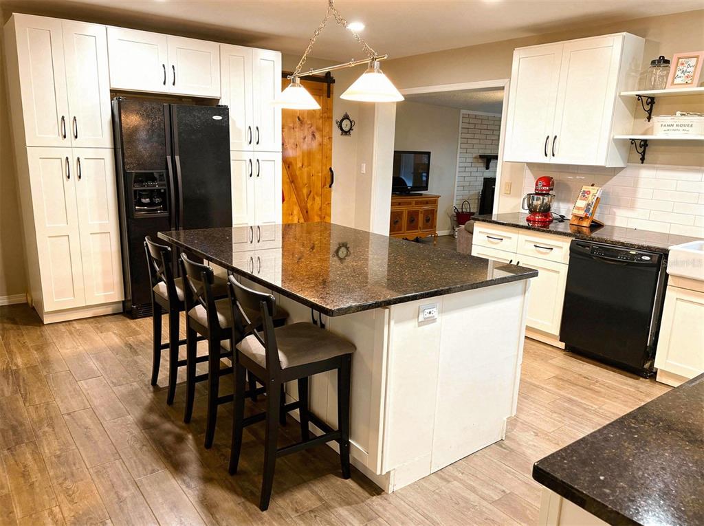A kitchen features white cabinetry, a dark granite island with bar seating, and black appliances — 2009 NE 51ST PLACE, OCALA, FL
