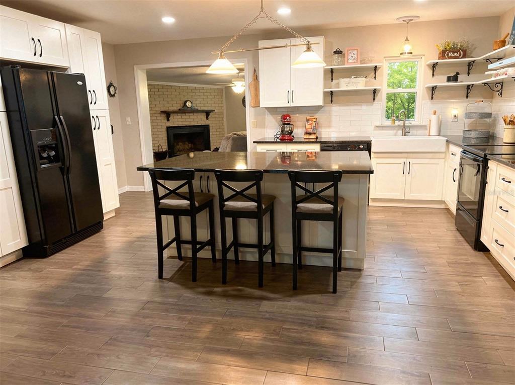 A kitchen features a central island with three stools, white cabinetry, and wood-look tile flooring — 2009 NE 51ST PLACE, OCALA, FL