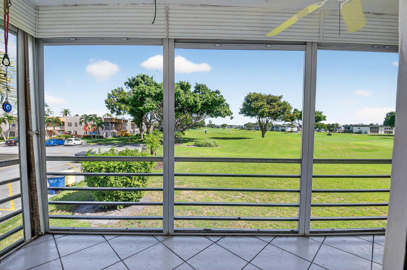 A screened-in balcony with tiled flooring overlooks a grassy golf course and parking area — 624 Flanders M, Delray Beach FL 33484, DELRAY BEACH, FL