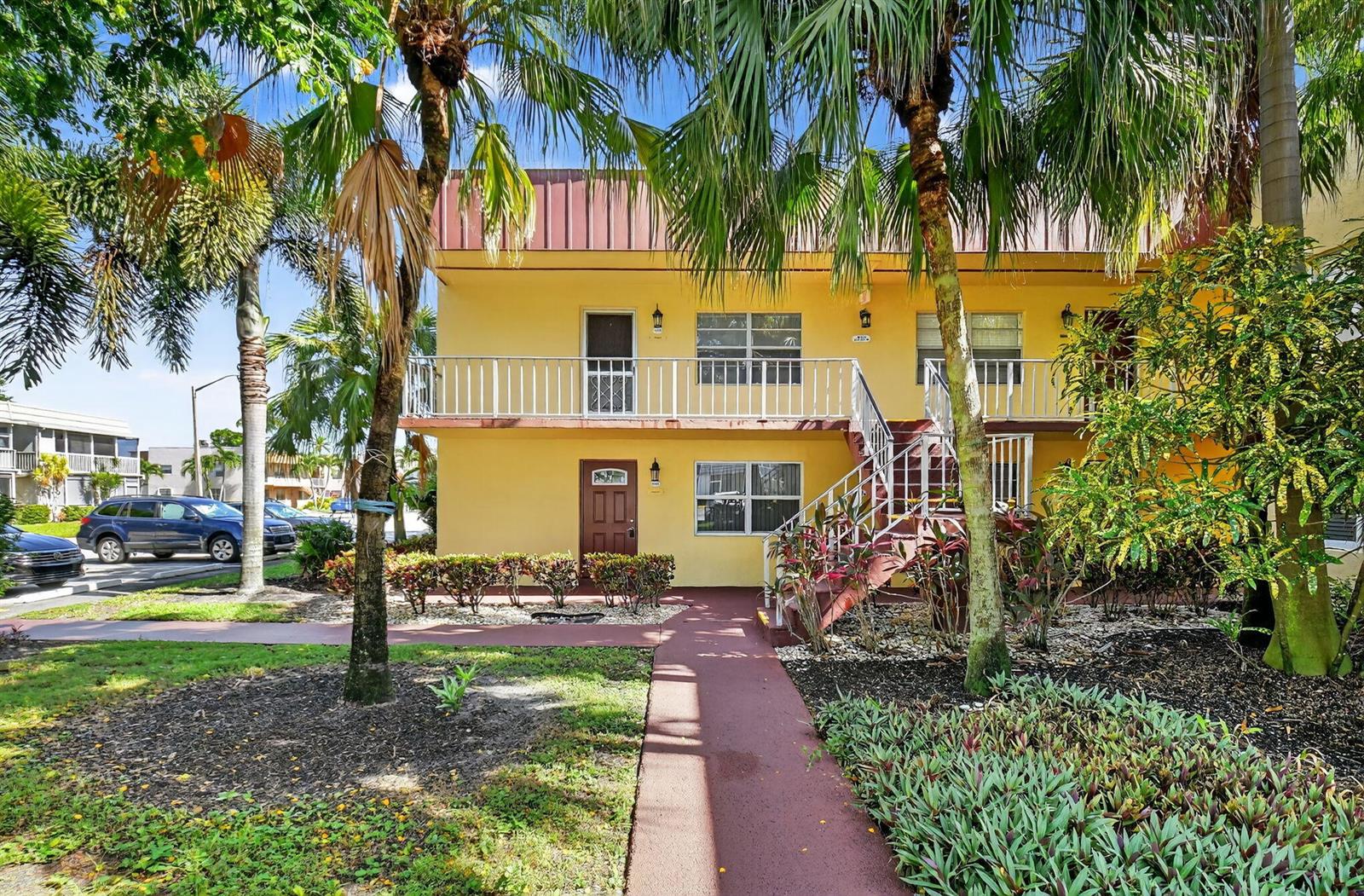 A two-story yellow apartment building with a balcony, exterior staircase, and palm trees in front — 624 Flanders M, Delray Beach FL 33484, DELRAY BEACH, FL