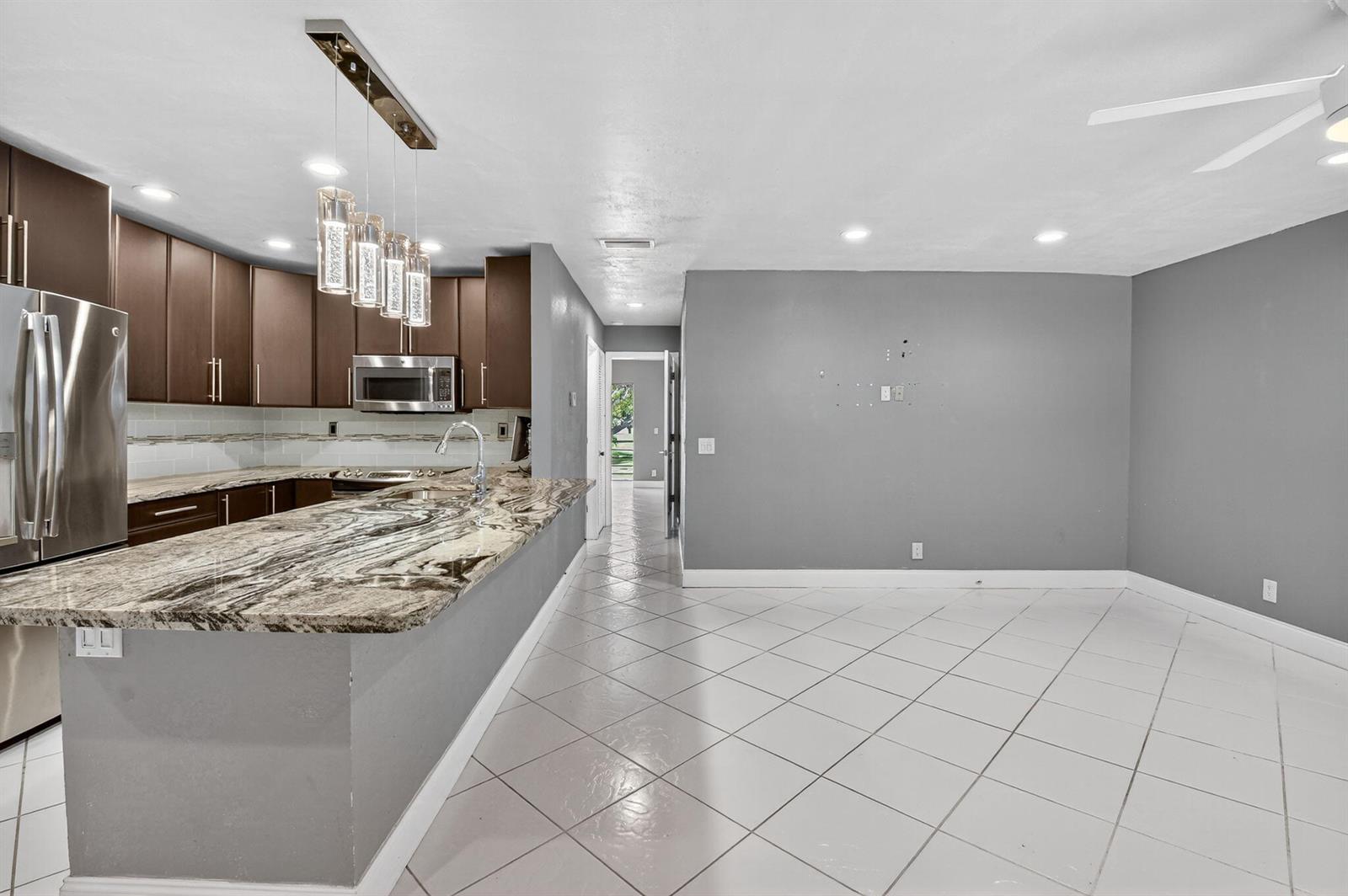 A kitchen with dark wood cabinets, granite countertops, and tile flooring opens to a dining area — 624 Flanders M, Delray Beach FL 33484, DELRAY BEACH, FL
