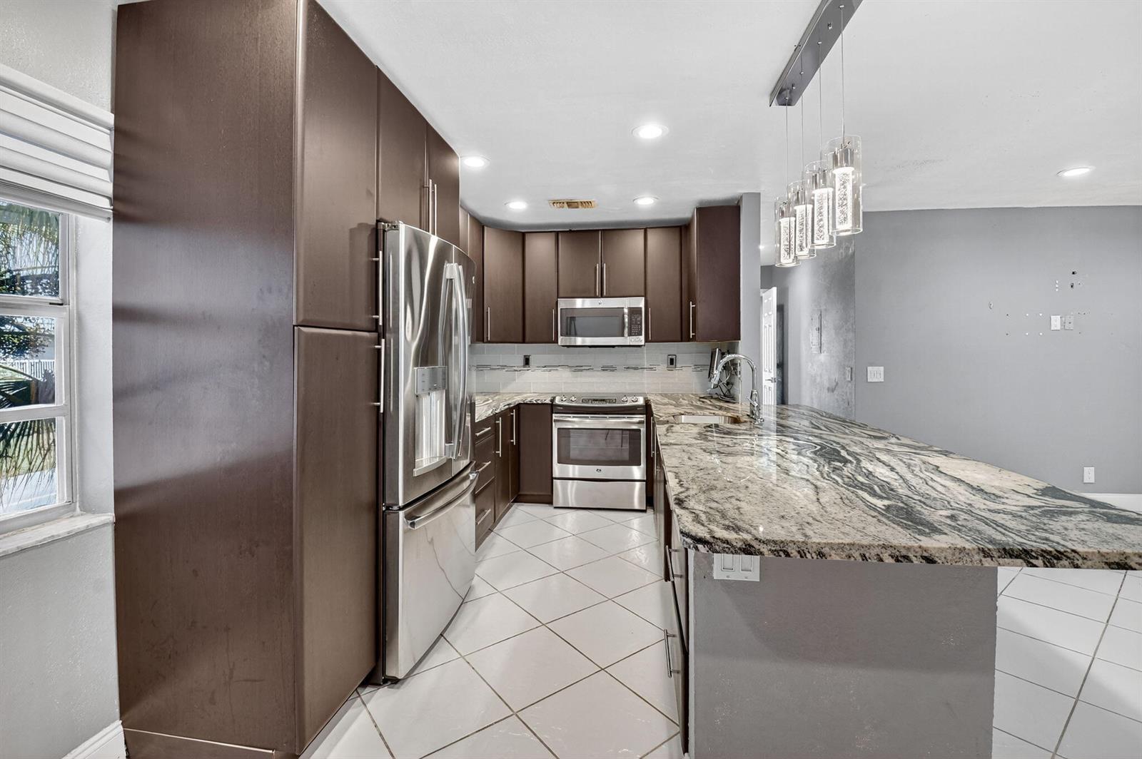 A kitchen with dark wood cabinets, stainless steel appliances, and a granite-topped island — 624 Flanders M, Delray Beach FL 33484, DELRAY BEACH, FL